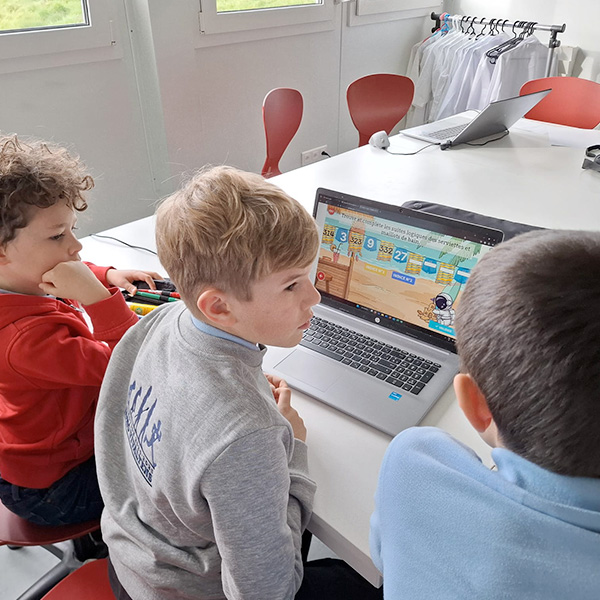 Trois élèves de Vivalys concentrés devant un ordinateur portable, travaillant sur un jeu mathématique.