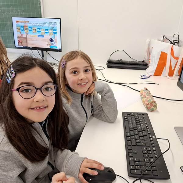 Deux jeunes élèves en train de travailler sur un exercice de logique mathématique sur un ordinateur de bureau.